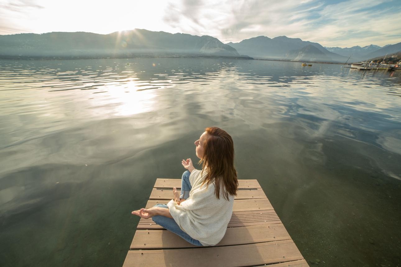 Woman meditating on a lakeside dock at sunrise